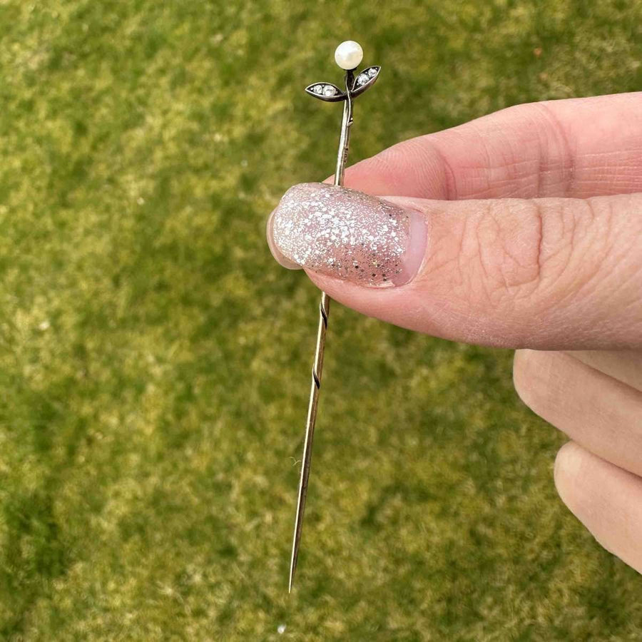 Close-up of Austro-Hungarian 14ct gold floral tie pin with pearl and rose-cut diamond, held delicately by a hand.