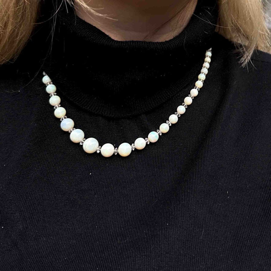 Early 20th century graduated opal bead necklace with a black turtleneck, showcasing enchanting hues and clarity.