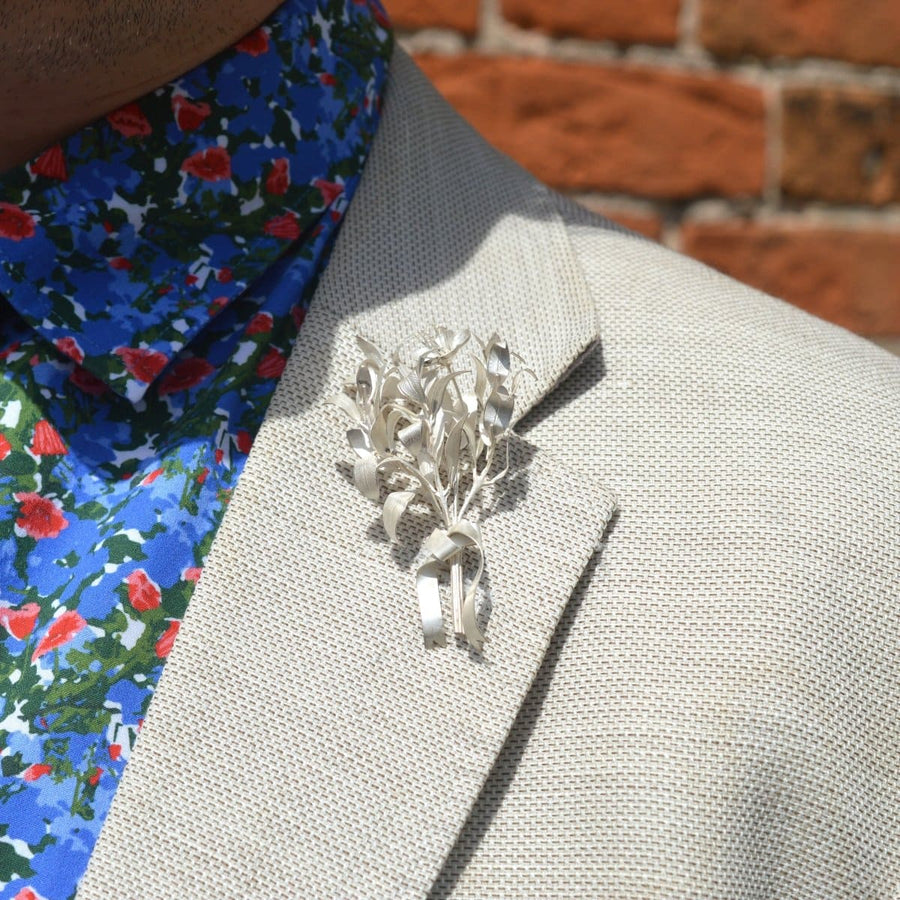 Elegant silver leaf corsage pin brooch on a textured blazer lapel, complemented by a colorful floral shirt.