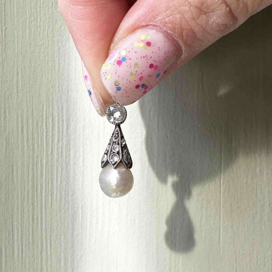 Victorian silver pendant featuring a natural saltwater pearl and diamond cone, held delicately by a hand.
