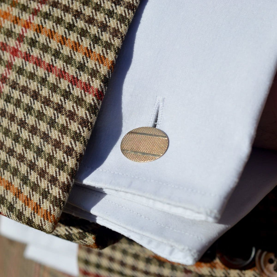 1960s 9ct gold engine turned cufflinks featured on a white shirt cuff against a textured patterned blazer.