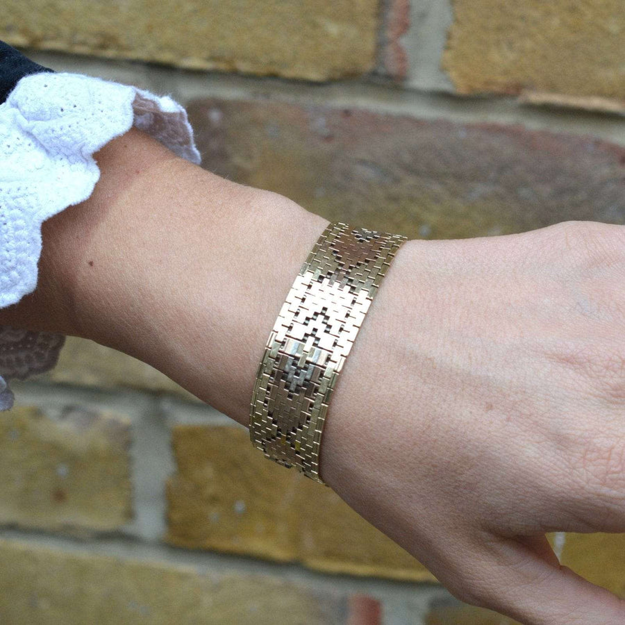 1970s three-colour 9ct gold weave bracelet worn on a wrist against a brick wall.