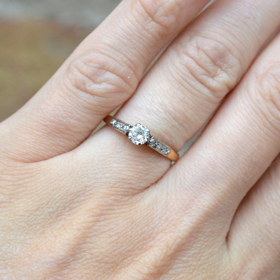 Art Deco 18ct Gold & Platinum diamond solitaire ring with diamond shoulders on a hand.