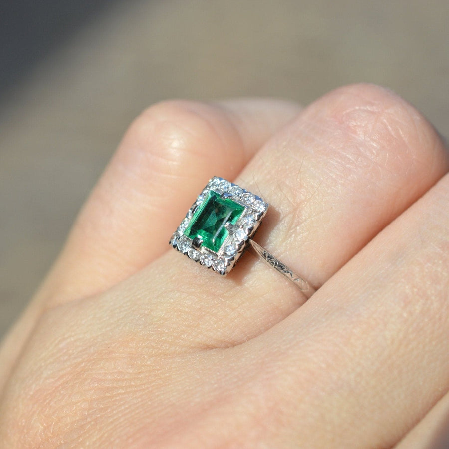 Art Deco platinum rectangular emerald and diamond cluster ring on hand, showcasing vibrant emerald and intricate engraving.