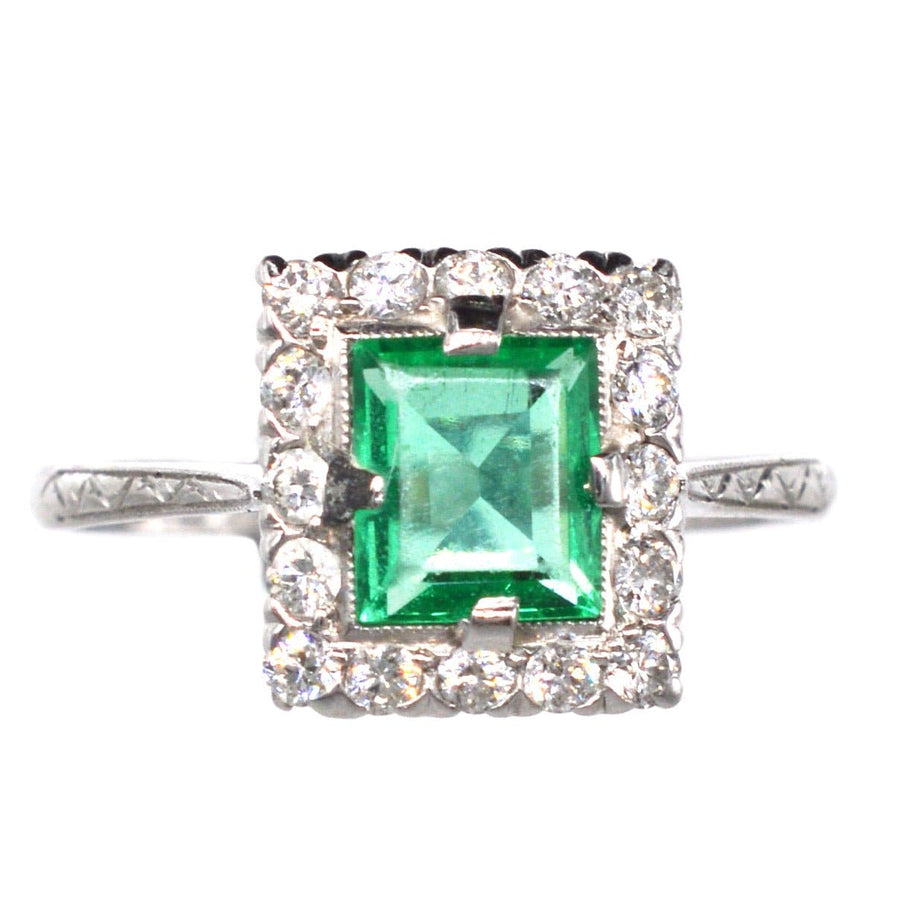Art Deco platinum ring featuring a vibrant rectangular emerald surrounded by a diamond cluster.