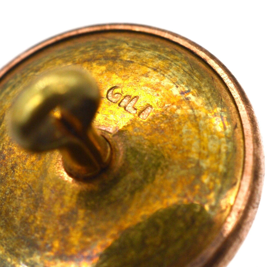 Close-up of the engraved base of a gilt button with a metal hook, displaying intricate gold tones.