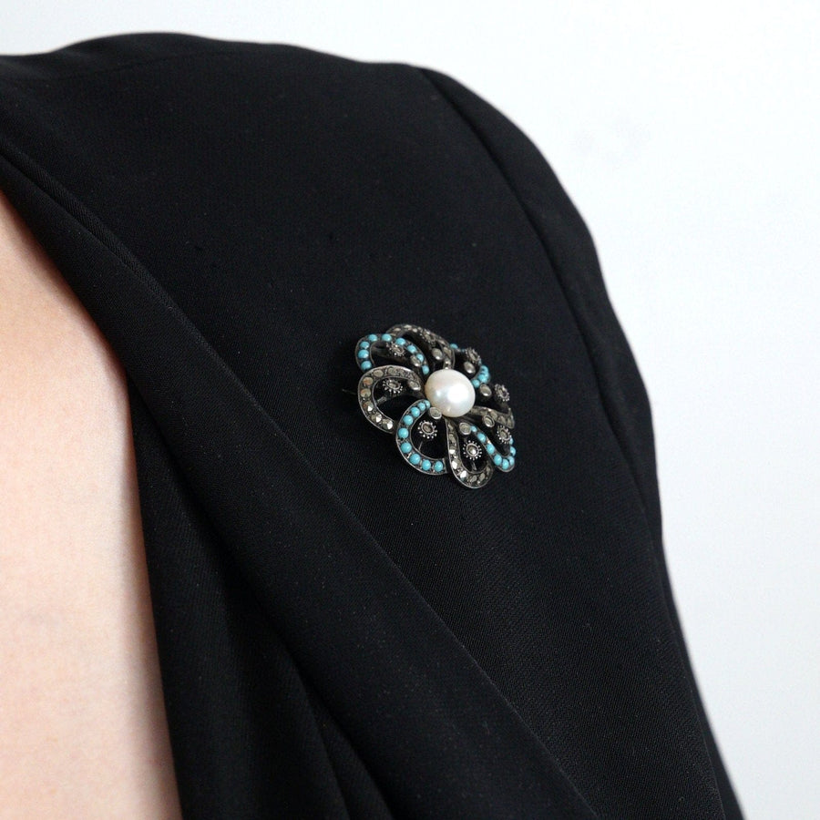 Art Deco silver marcasite turquoise cultured pearl brooch on a black garment, showcasing vintage elegance.