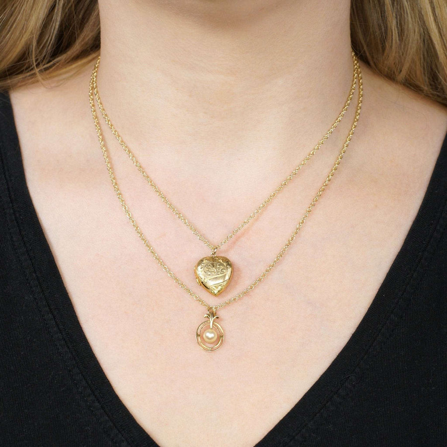 Layered gold necklaces featuring a heart and oval pendant on a model's neck.