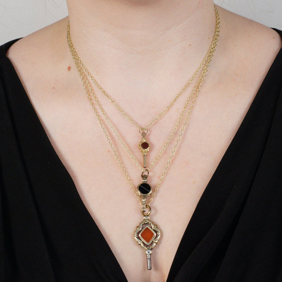 Layered gold necklaces featuring black and orange gemstones, elegantly worn on a model's neck.
