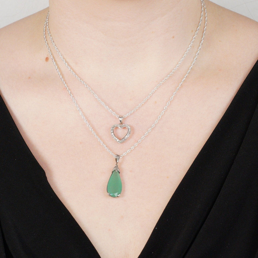 Layered silver necklaces with heart and teardrop pendants displayed on a model.