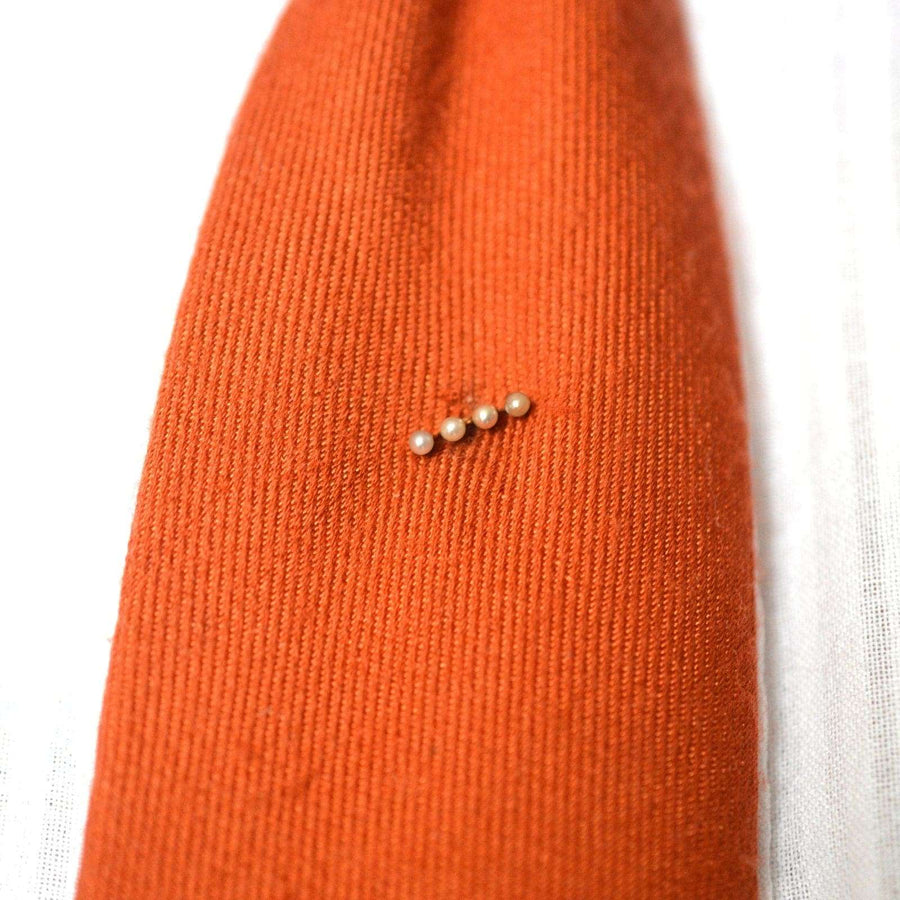 Edwardian 15ct gold tie pin featuring four natural pearls on an orange silk tie, adding elegance to formal attire.