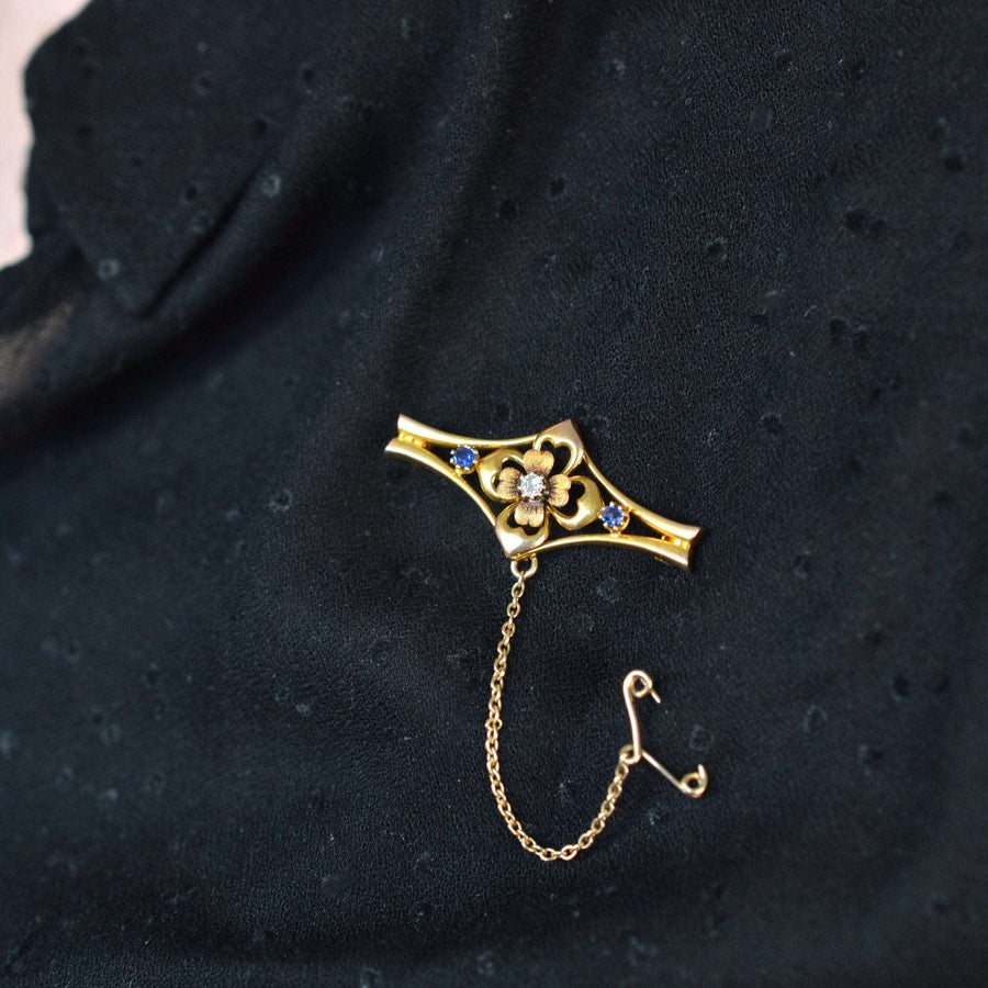 Edwardian 15ct gold floral bar brooch with sapphire and diamond accents on black fabric.