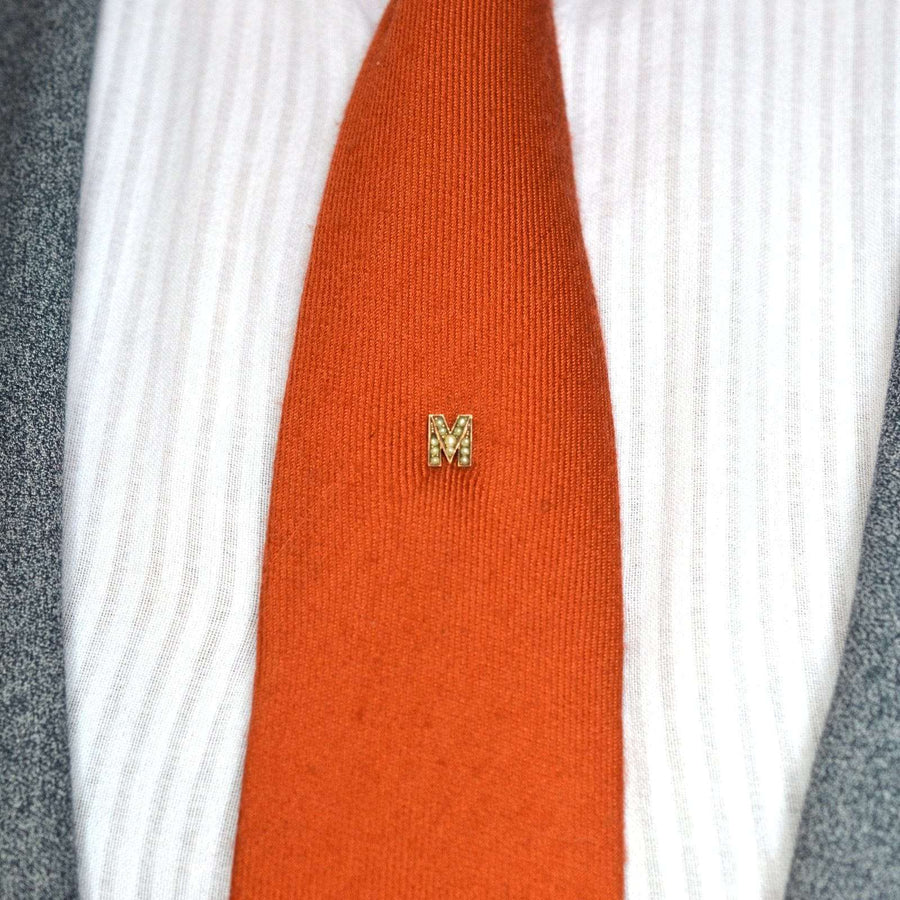 Edwardian 15ct gold seed pearl letter 'M' tie pin on orange silk tie, elegant men's accessory.
