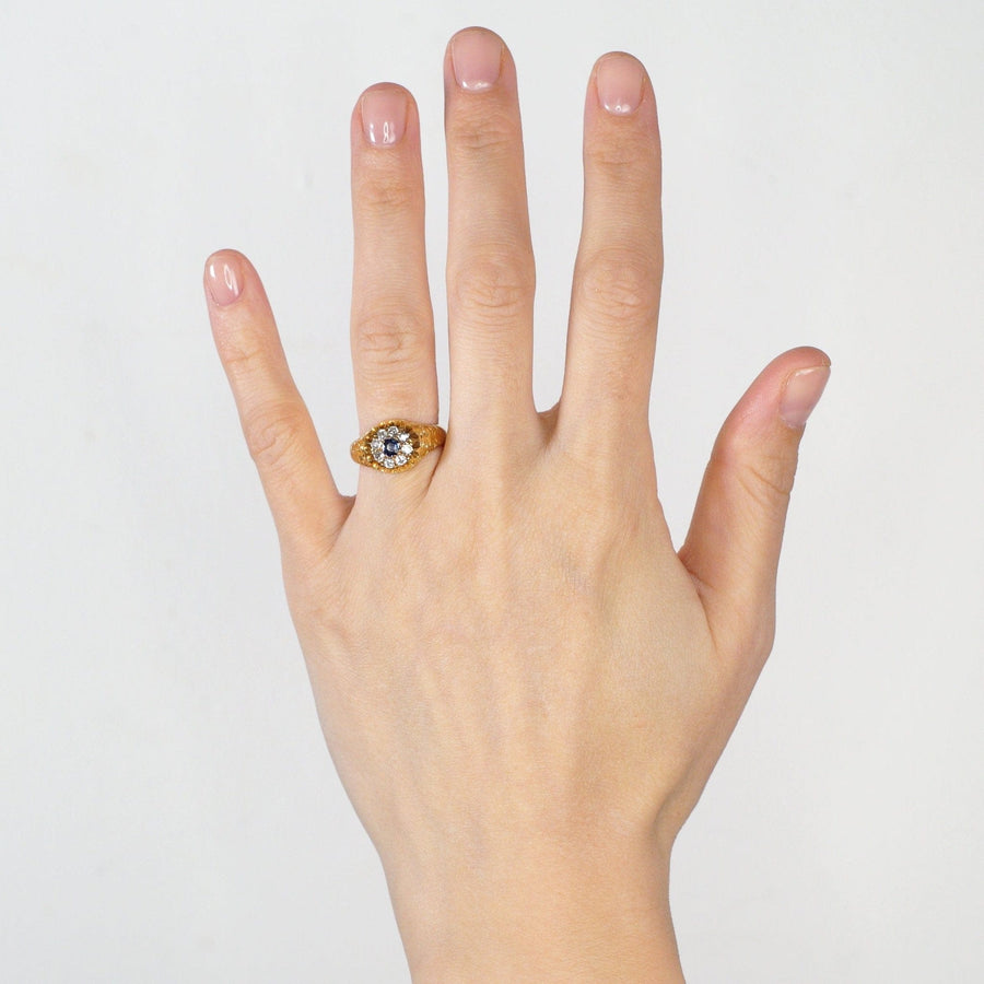 Edwardian 18ct gold cluster ring featuring old mine cut diamonds and a vibrant sapphire, displayed on a hand.