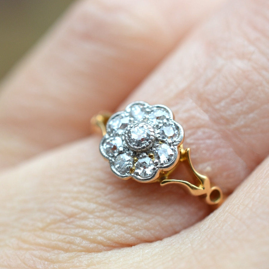 Edwardian 18ct gold cluster ring featuring a flower-shaped design with old mine cut diamonds and decorated shoulders.