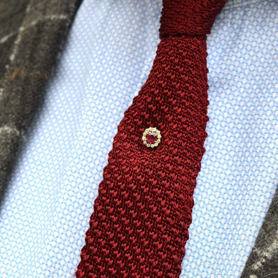 Close-up of an Edwardian tie pin featuring a ruby and diamond cluster on a textured maroon tie.