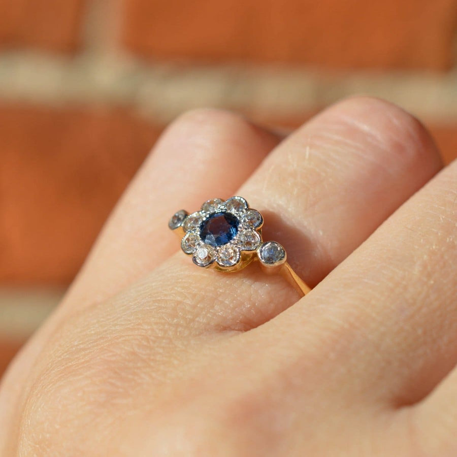 Edwardian 18ct gold and platinum sapphire diamond cluster ring on finger, featuring blue sapphire and diamond halo.
