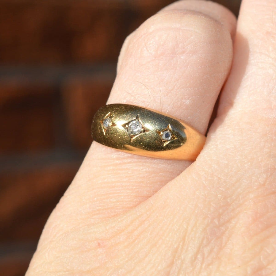 Edwardian 18ct gold three stone gypsy ring with diamonds, unique vintage jewelry worn on a hand against a blurred background.