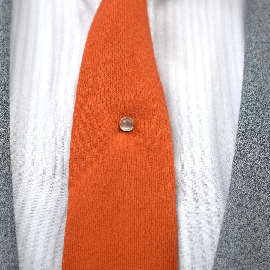 18ct gold tie pin with moonstone on an orange tie against a gray suit.
