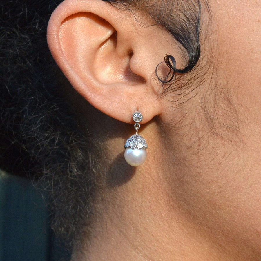 Edwardian 18ct white gold earrings featuring a cultured pearl and rose diamond accent, elegantly worn.