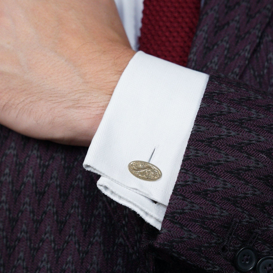 Close-up of a hand wearing 1890-1910 Edwardian 9ct gold cufflinks with foliage design on a white shirt.