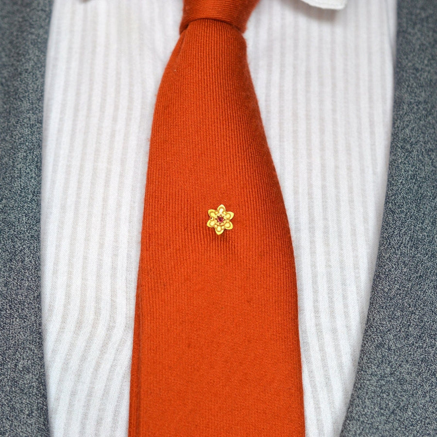 Edwardian 9ct gold flower tie pin with ruby on a vibrant orange tie, showcasing vintage elegance.