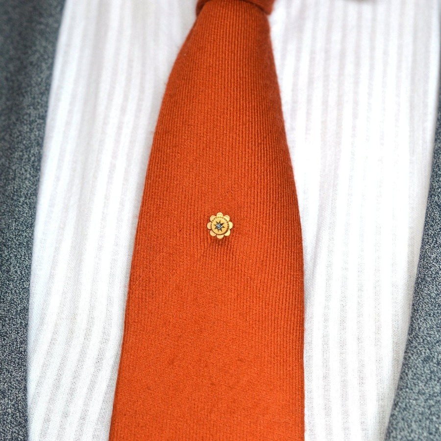 Edwardian 9ct gold flower tie pin with sapphire on an orange silk tie, adding elegance to formal attire.