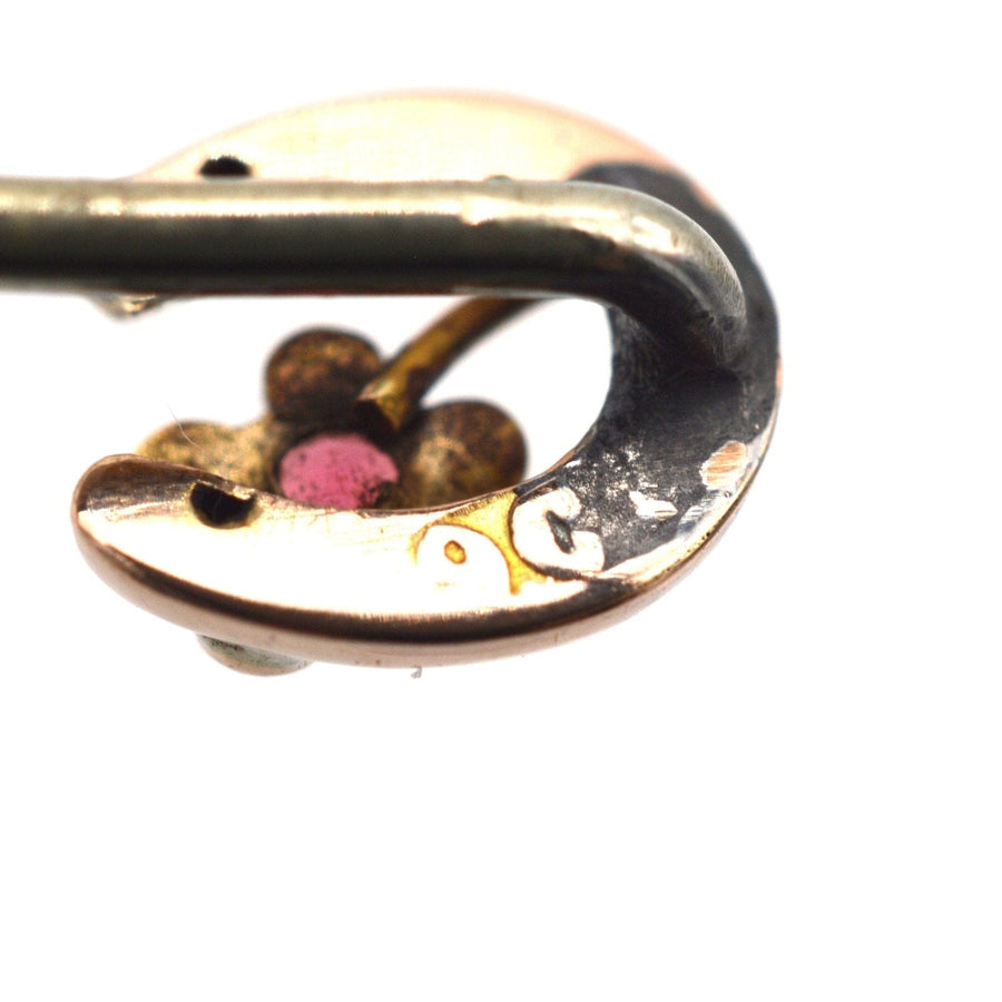 Close-up of an Edwardian 9ct gold horseshoe tie pin with flower and garnet accent, showcasing intricate design.