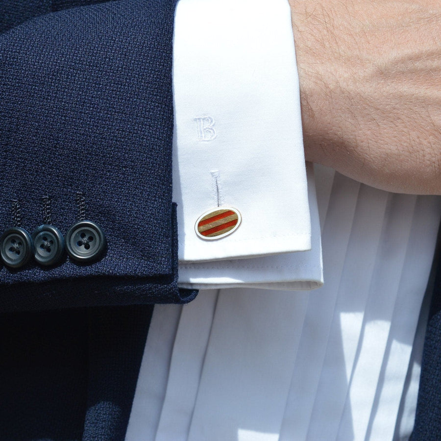 Elegant Edwardian 9ct gold oval cufflink with red striped enamel on a white dress shirt cuff.