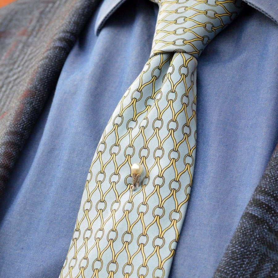 Edwardian natural pearl and diamond platinum tie pin on a patterned silk tie styled with a blue shirt.