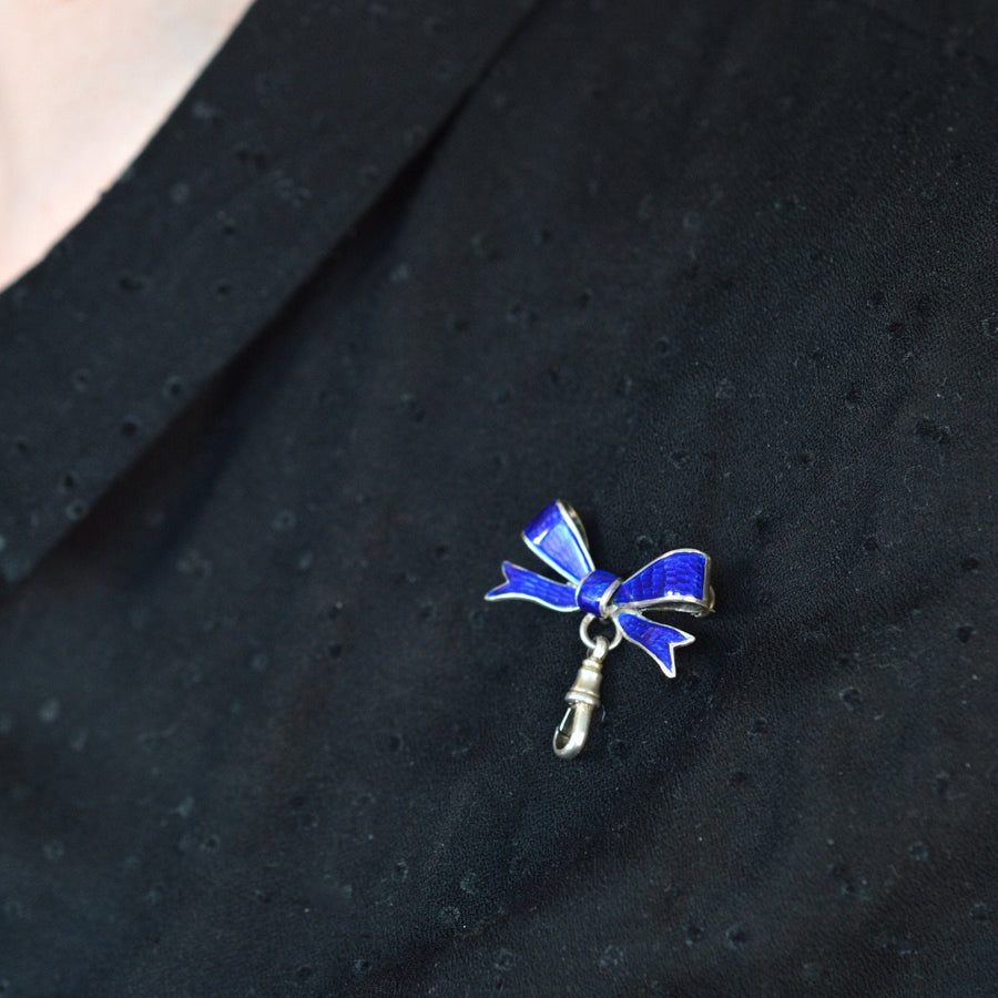 Edwardian royal blue guilloché enamel and silver bow brooch with dog clip, worn on a black blouse.