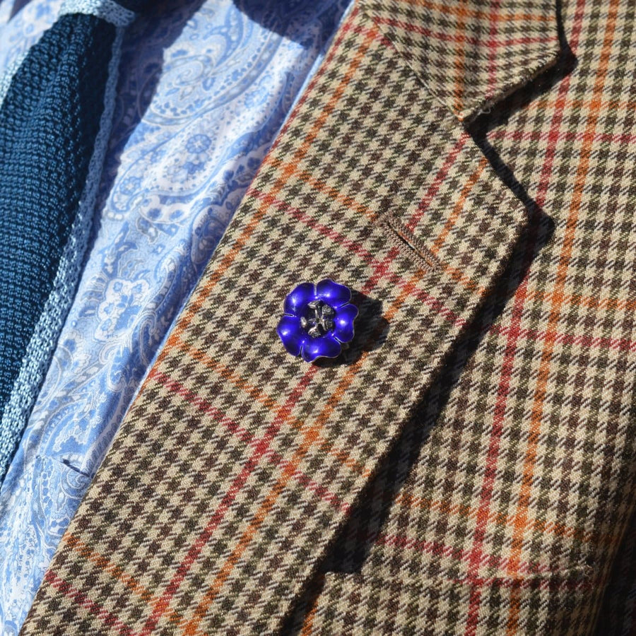 Edwardian silver blue enamel flower brooch on a checked jacket lapel, highlighting its cobalt petals and white paste stamens.
