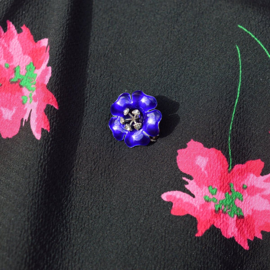 Edwardian silver brooch with cobalt blue enamel flower petals and white paste stamens on a floral background.