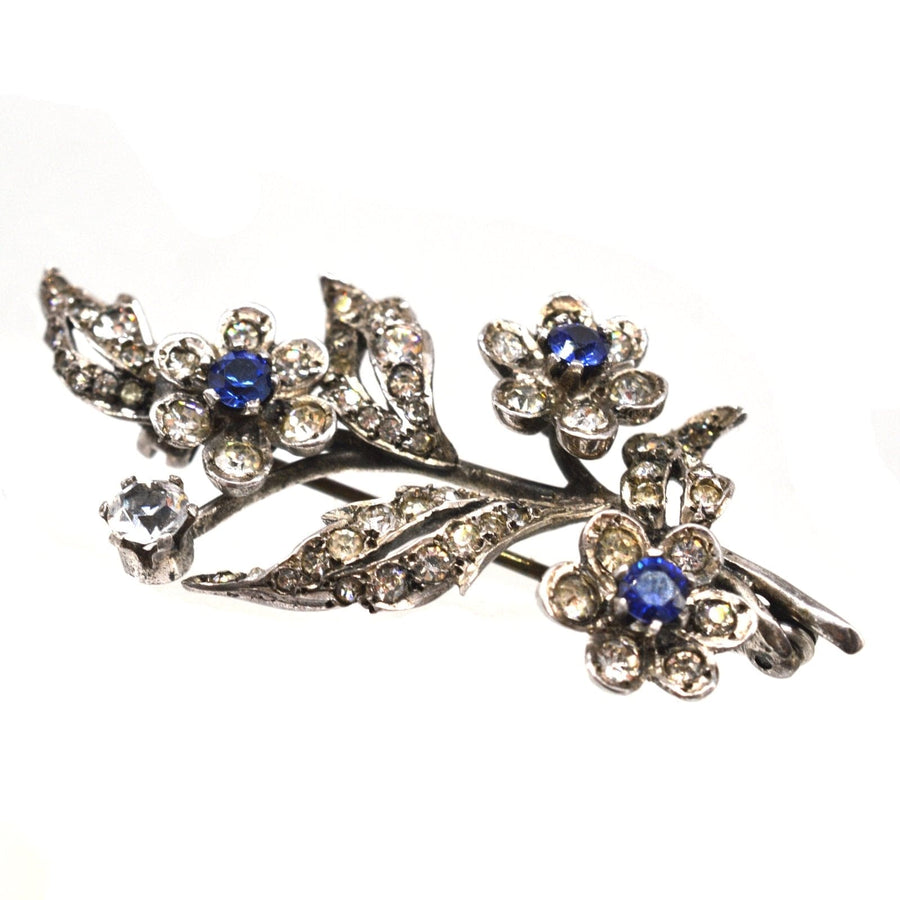 Edwardian silver floral brooch with blue sapphire and white paste stones, elegantly designed with sparkling details.