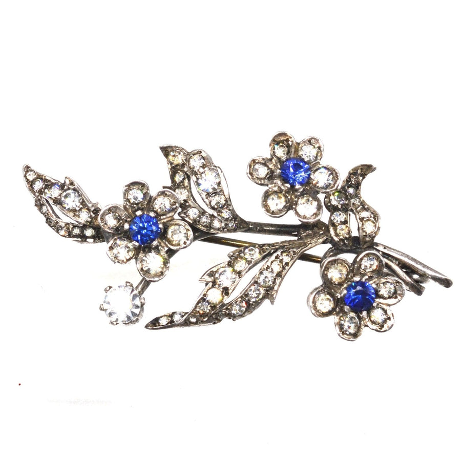 Edwardian silver floral brooch with blue sapphire and white paste stones, combining elegance and vintage charm.