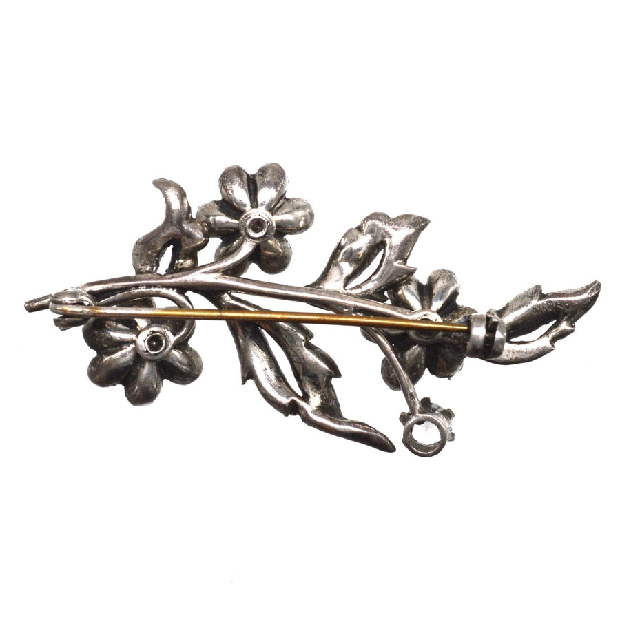 Edwardian silver floral brooch with blue sapphire and white paste accents, featuring intricate leaf and flower design.