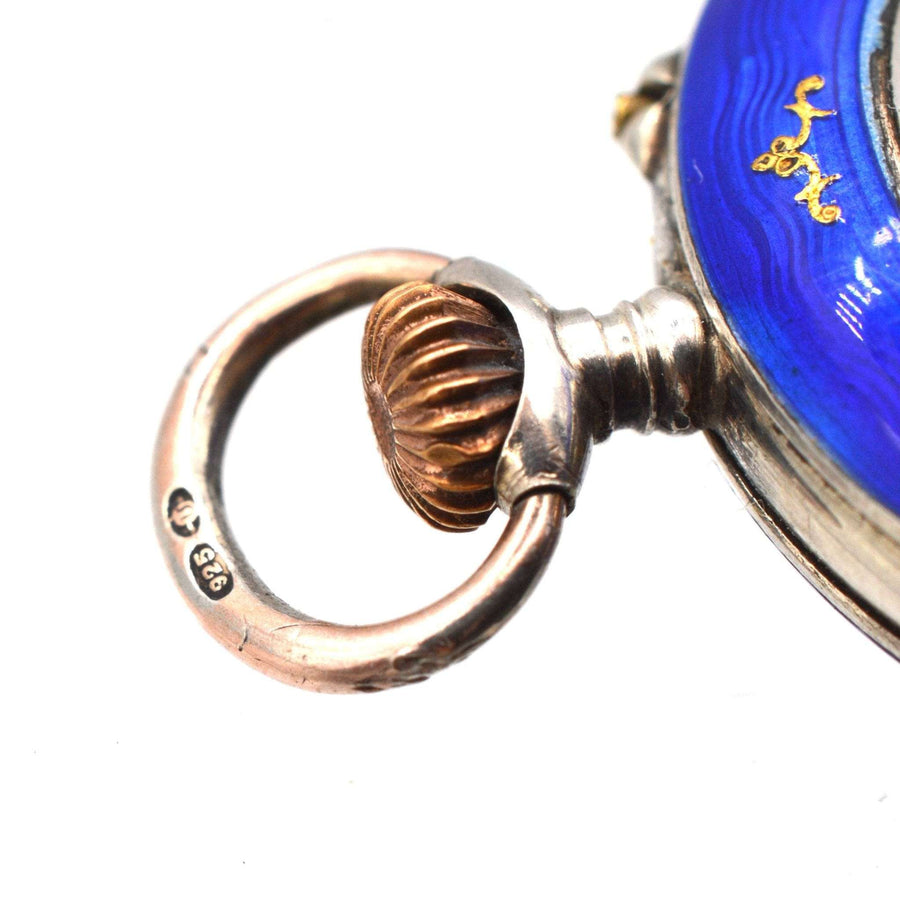 Close-up of Edwardian silver pocket watch with royal blue guilloché enamel and ornate crown, showcasing intricate craftsmanship.