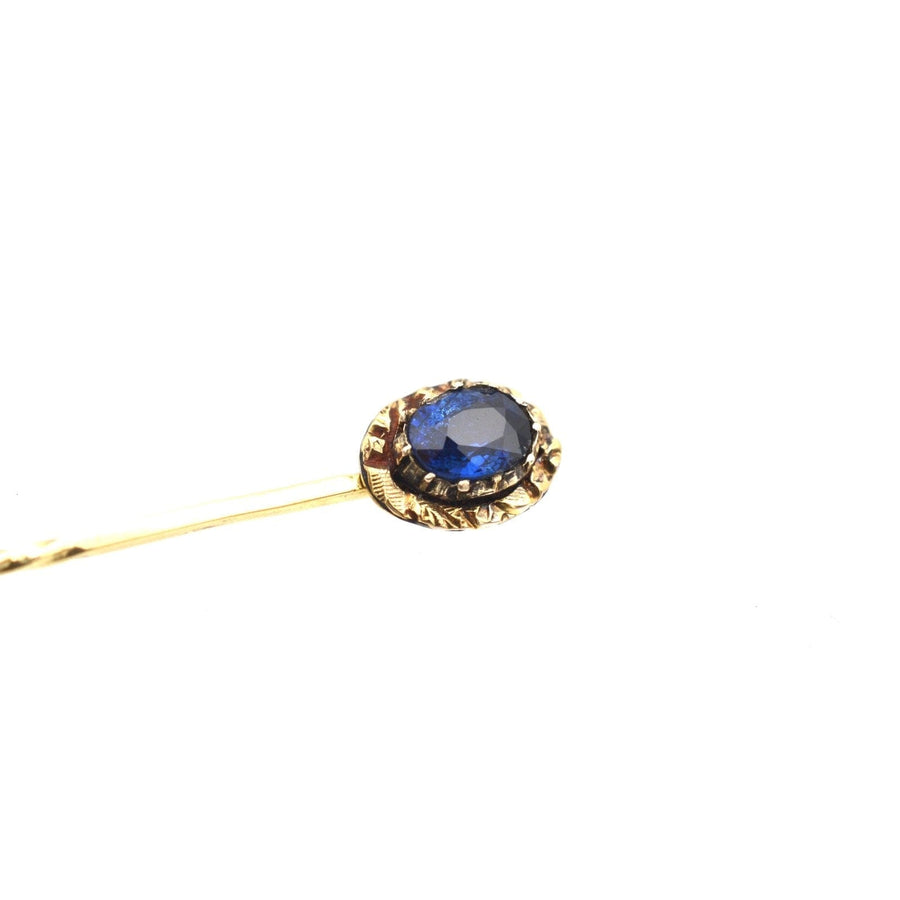 Georgian 15ct gold tie pin featuring a blue sapphire at the center with ornate repoussé detailing.
