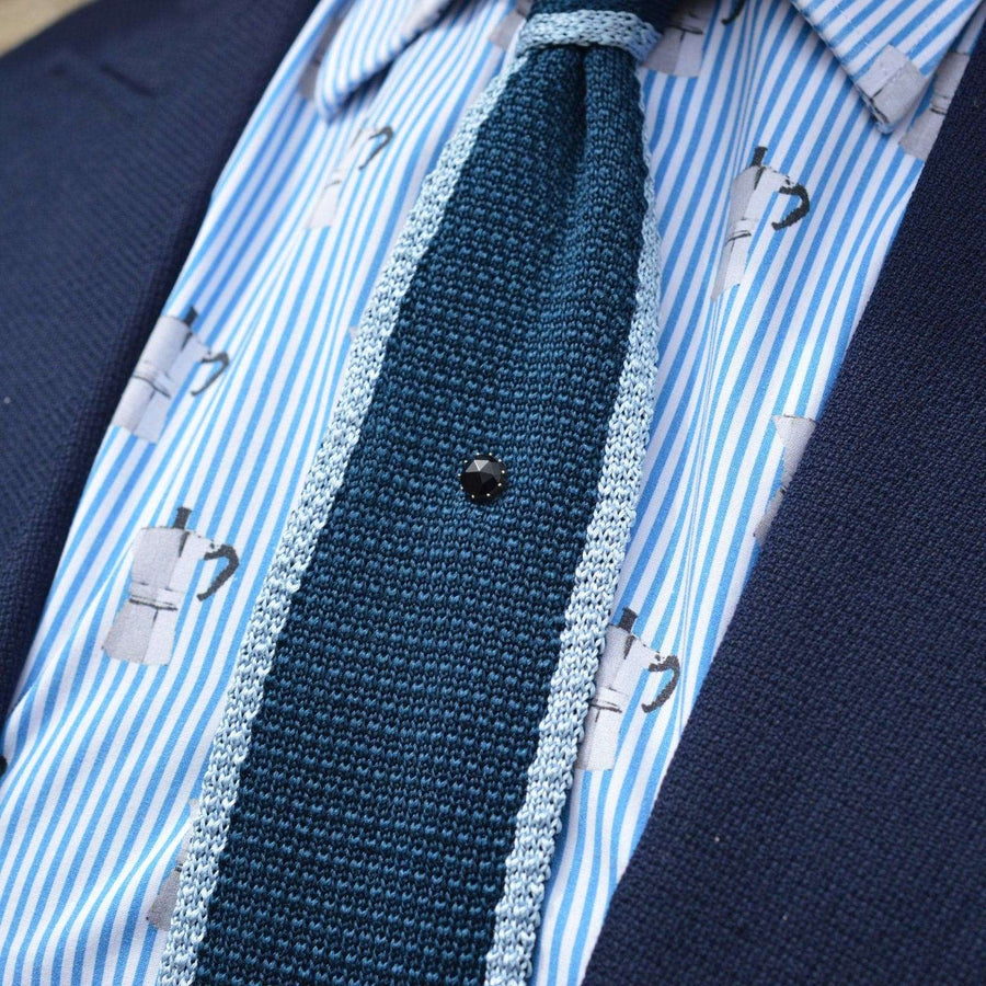 Close-up of a Georgian 9ct gold tie pin featuring Vauxhall glass on a blue knit tie against a striped shirt.