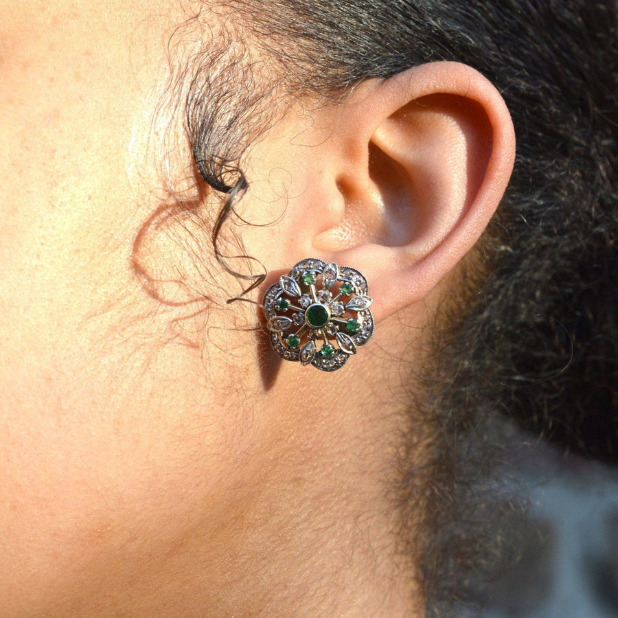 Large 1950s gold emerald and diamond cluster stud earrings worn by a model, showcasing floral design and elegance.
