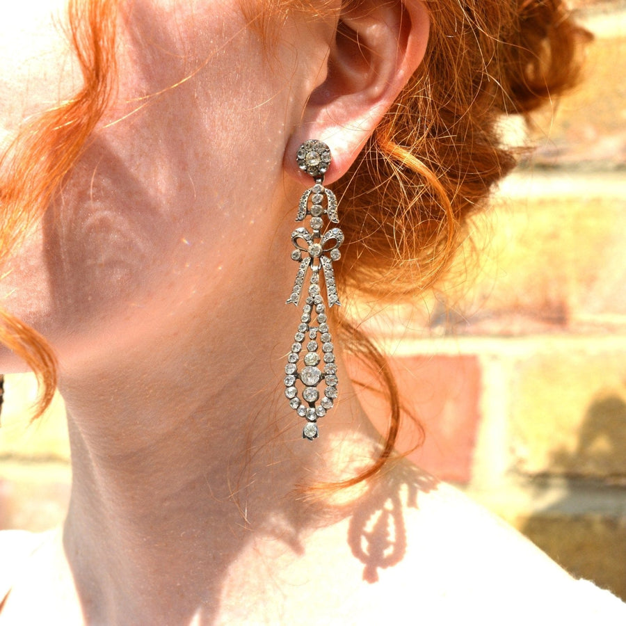 Large 19th century silver Portuguese style pendeloque bow paste earrings worn by a model with red hair.