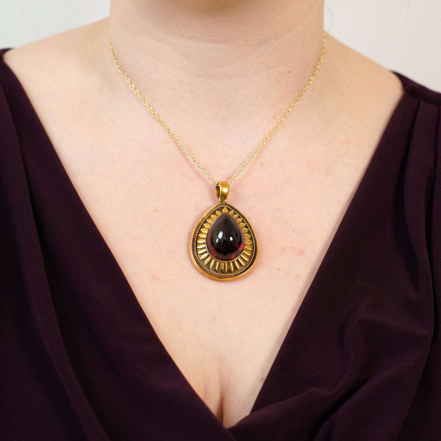 Large gold pendant with a cabochon garnet, worn on a model's neck, showcasing antique jewelry style.