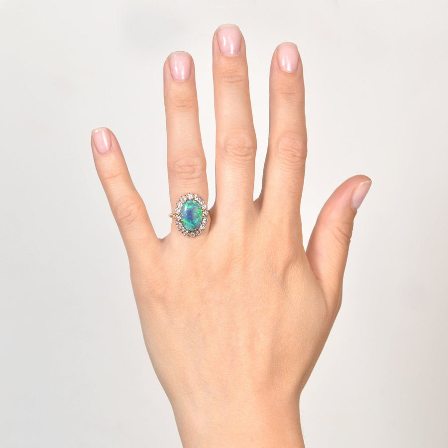 Large Victorian 18ct gold black opal and diamond cluster ring worn on a woman's hand, showcasing its vibrant colors.