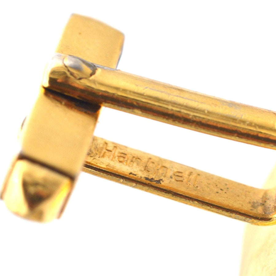 Close-up of a vintage Norman Hartnell cufflink showcasing intricate gold detailing and brand engraving.