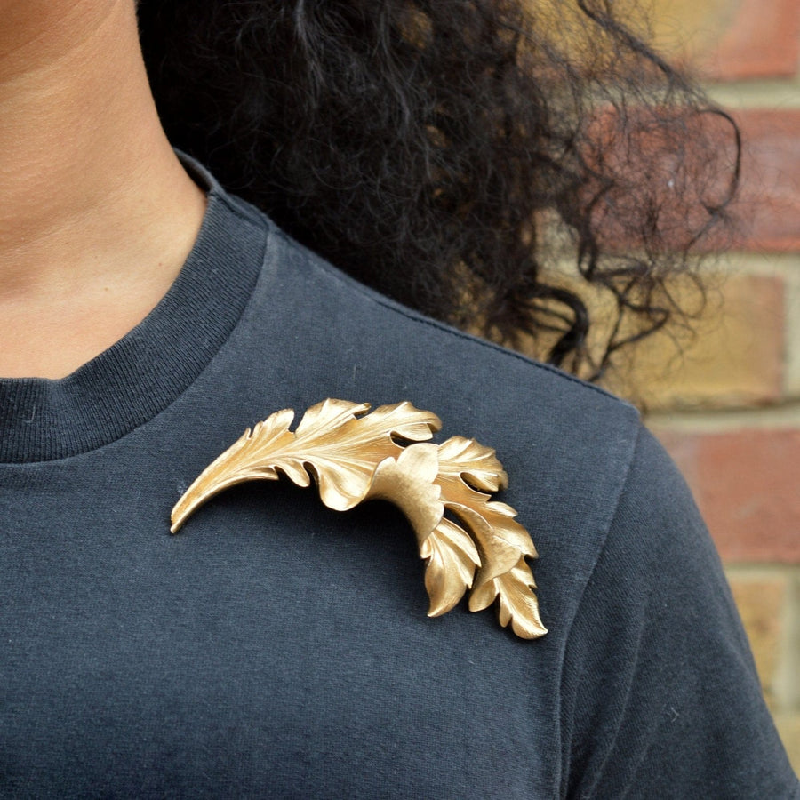 Mid Century Trifari large gilt metal leaf brooch worn on a dark shirt, showcasing its elegant design and vibrant gold color.