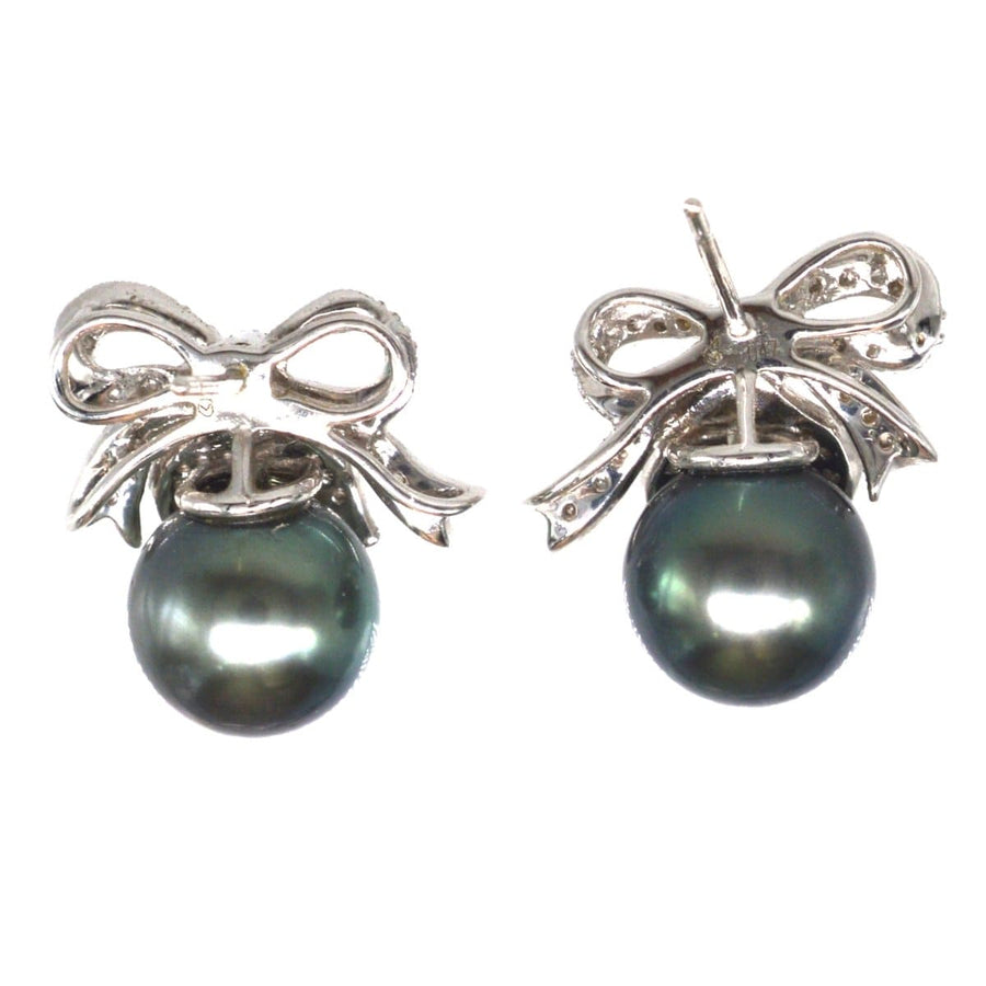 Chic black pearl stud earrings with diamond bow accents, perfect for elegant occasions.