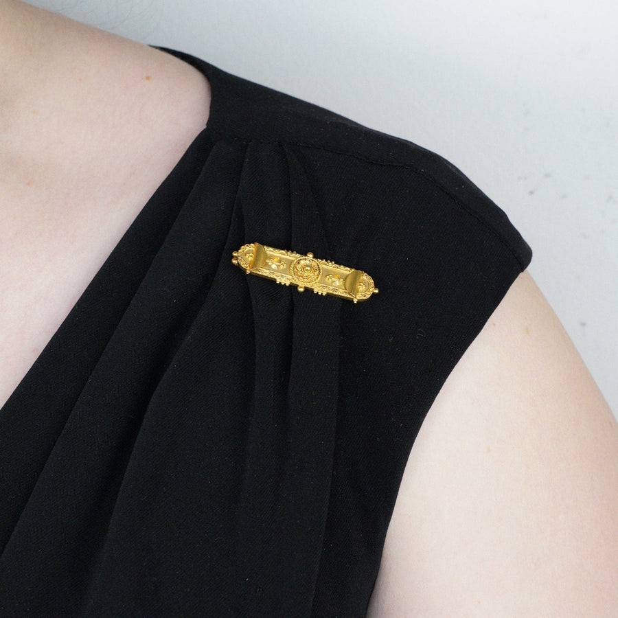 Victorian 15ct gold Etruscan Revival brooch displayed on a black dress shoulder, showcasing intricate design and elegance.