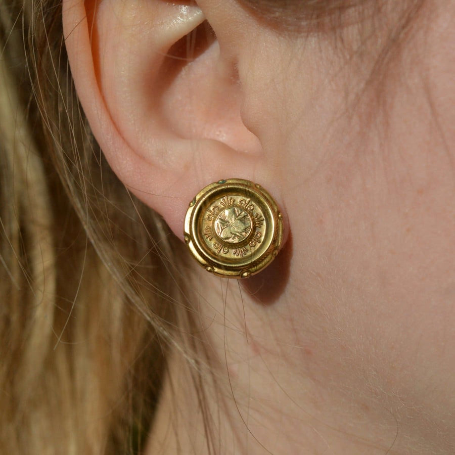 Gold round Etruscan style earrings displayed on a model's ear with intricate design features.