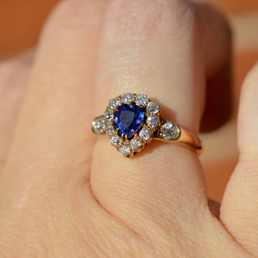 Victorian 18ct gold heart-shaped sapphire and diamond cluster ring showcased on a finger in sunlight.
