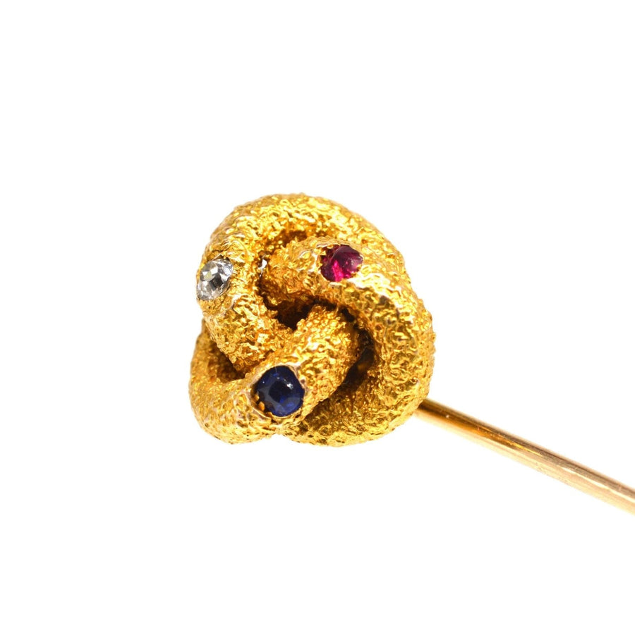 Victorian gold knot tie pin featuring a ruby, diamond, and sapphire, showcasing vibrant colors and fine craftsmanship.